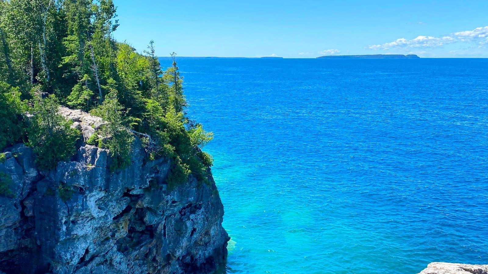 A limestone cliff covered in cedar and pine trees overlooking turquoise water and small islands on the Bruce Peninsula