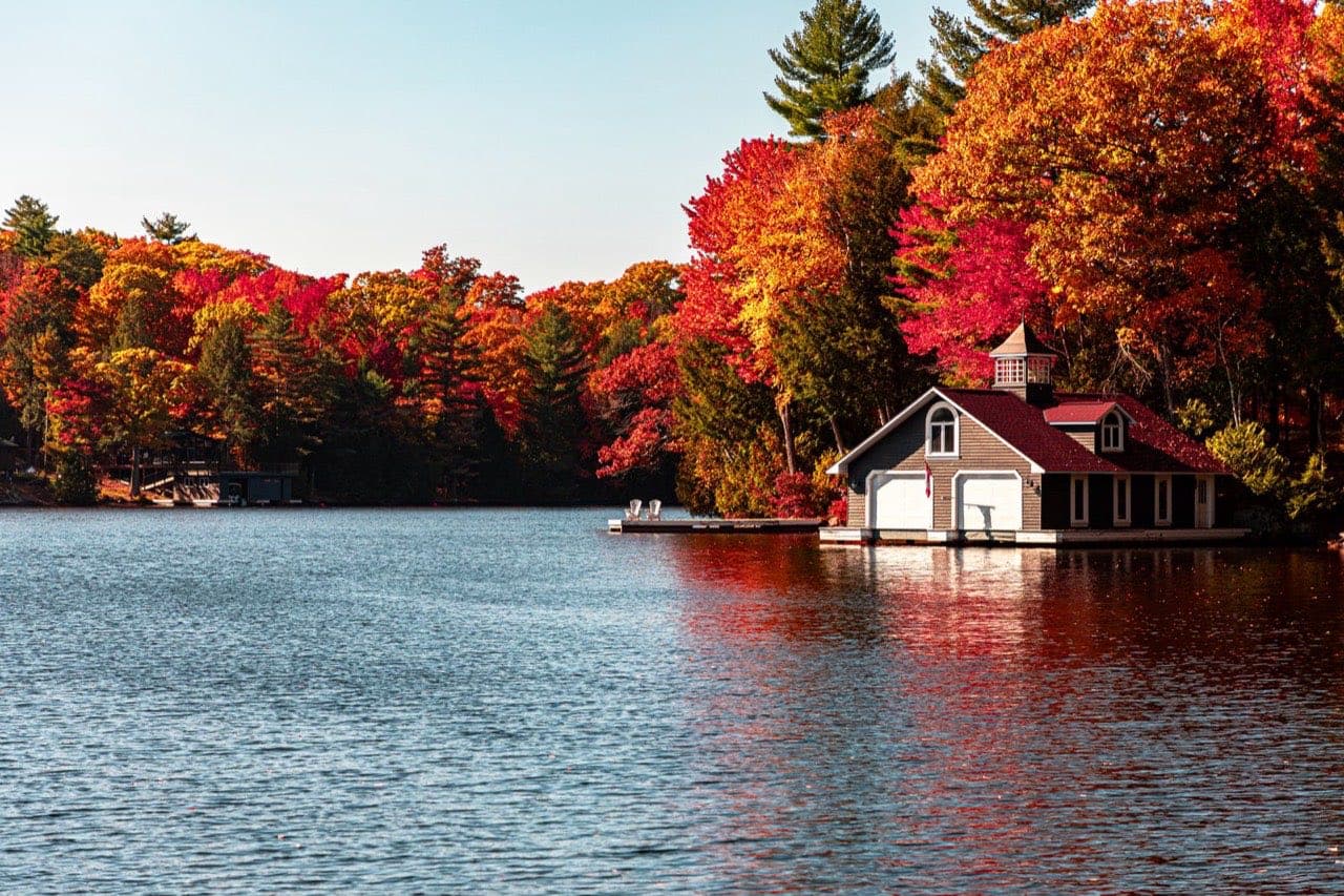 A lakeside cottage beside a calm lake, surrounded by trees in autumn color