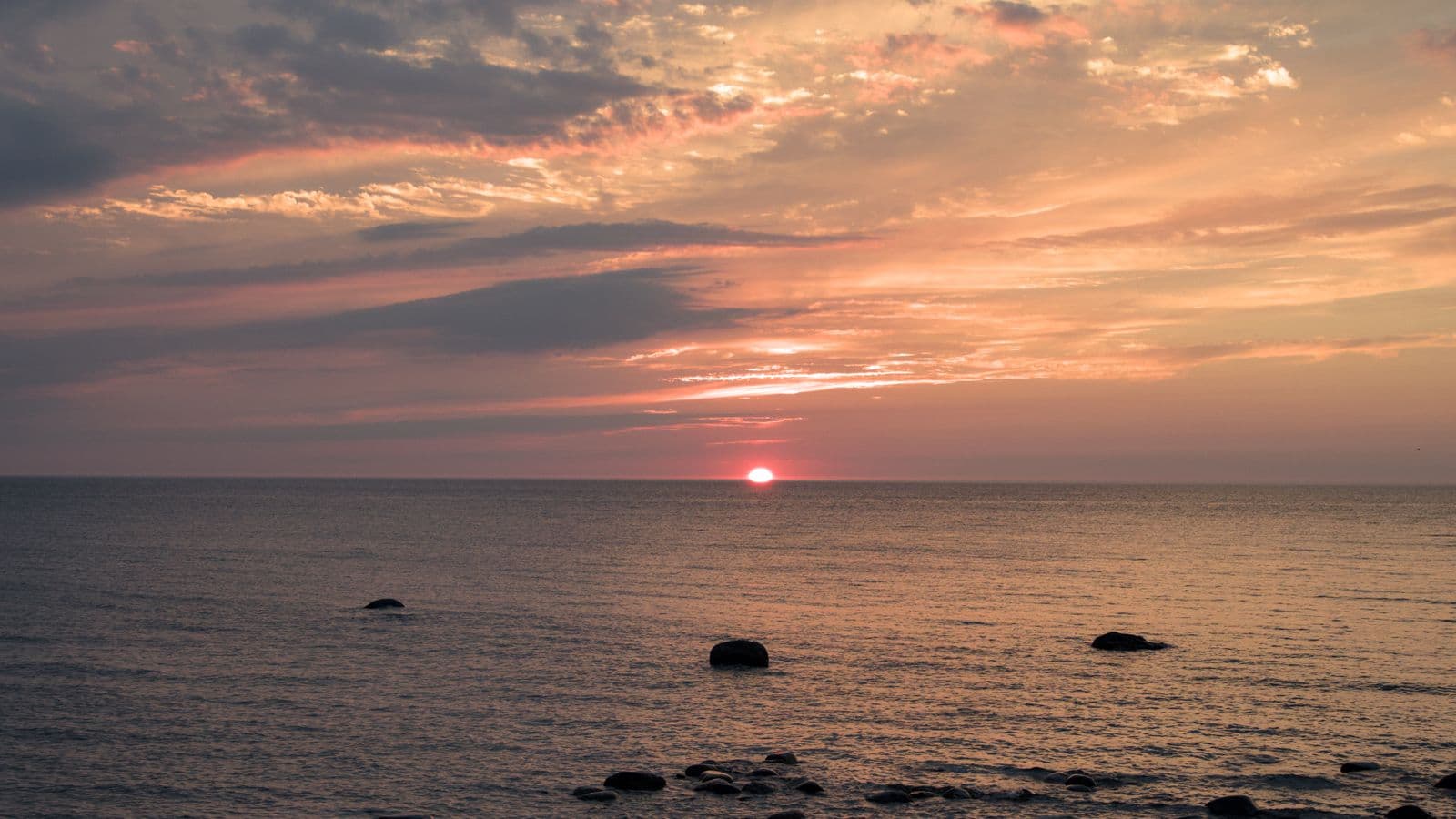 Sun setting over Lake Huron, with rocks scattered in the shallows near shore